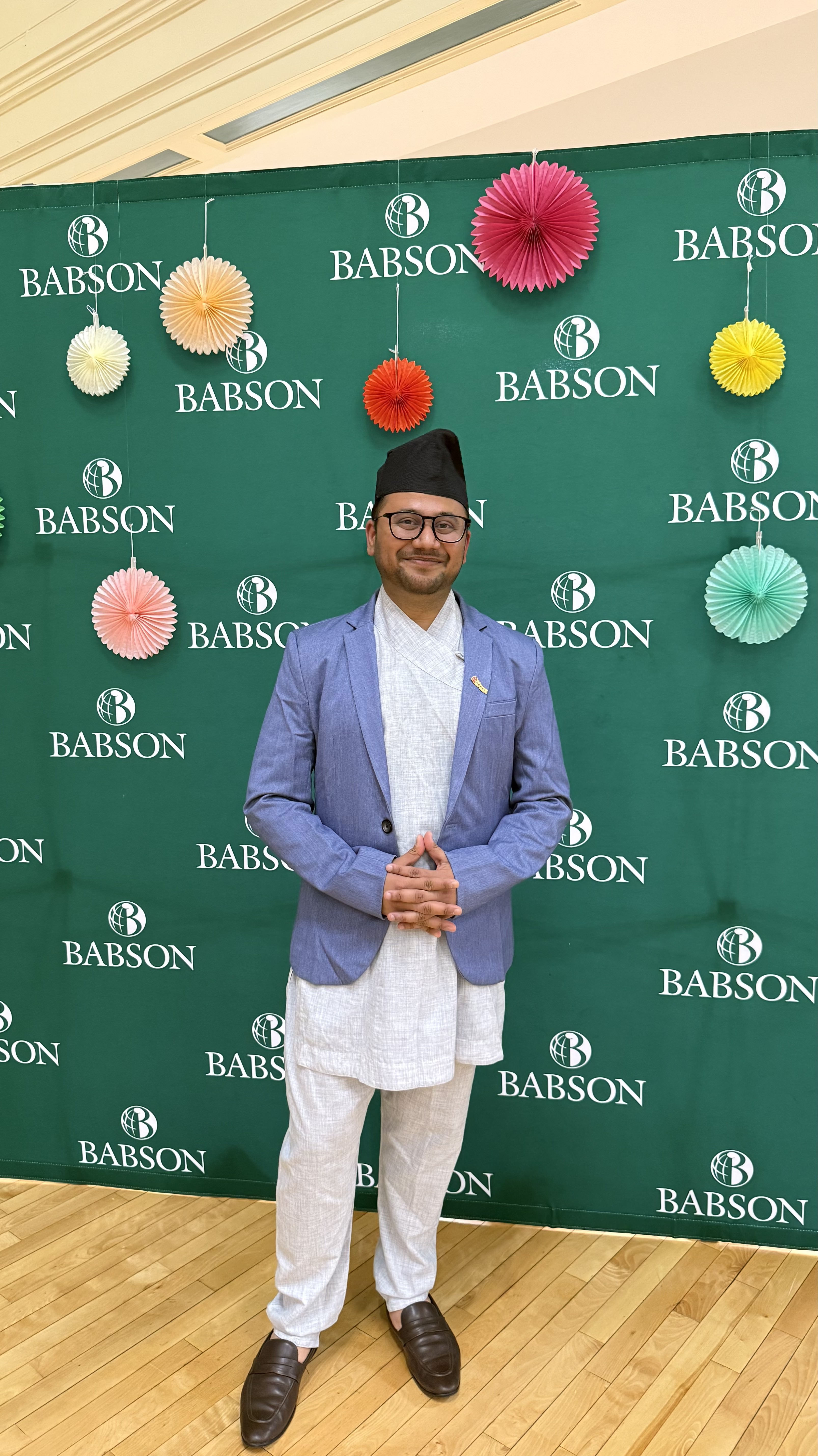 Person in traditional Nepali attire in front of Babson College backdrop