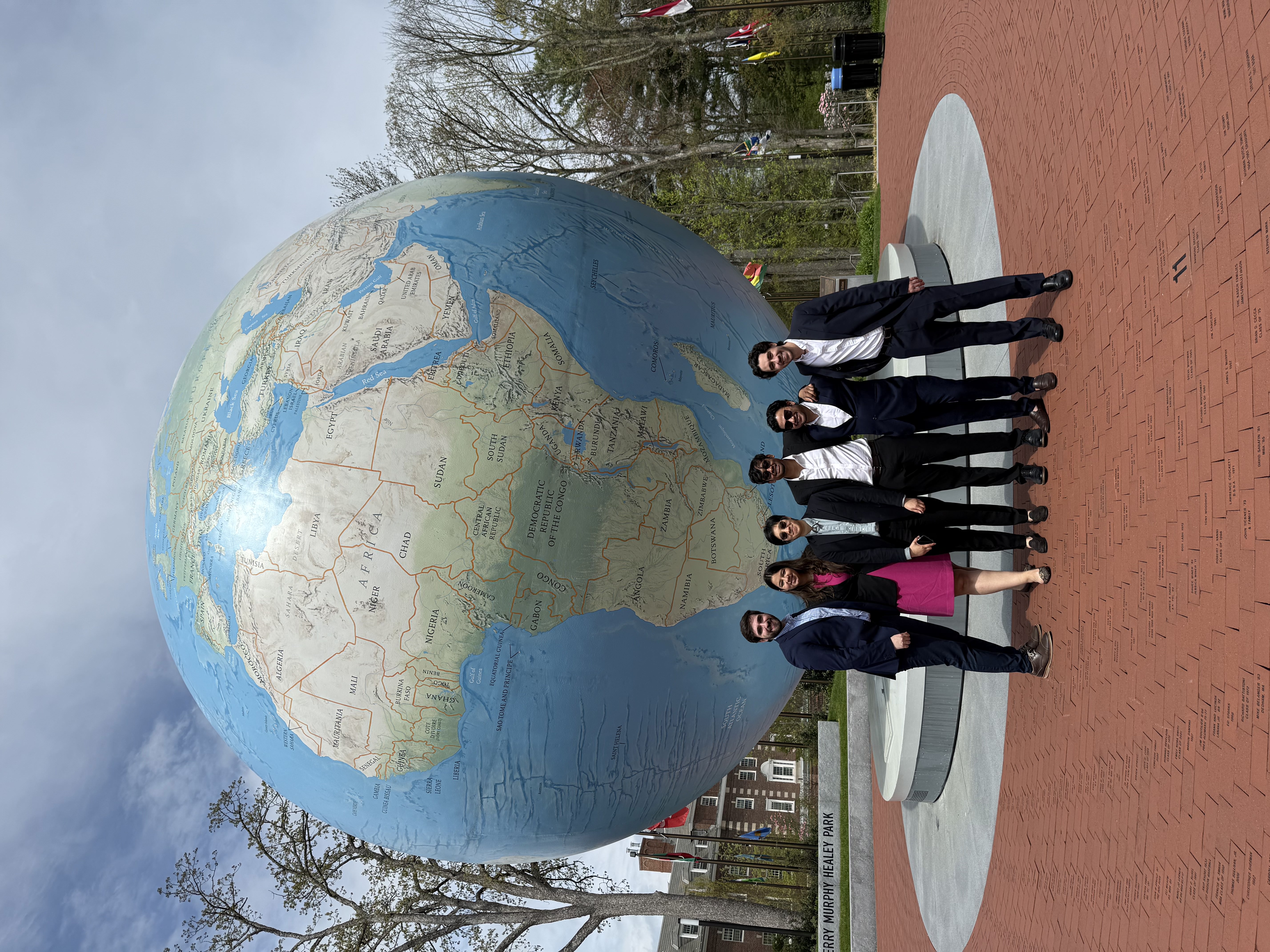 Five students in business attire posing at the Babson globe