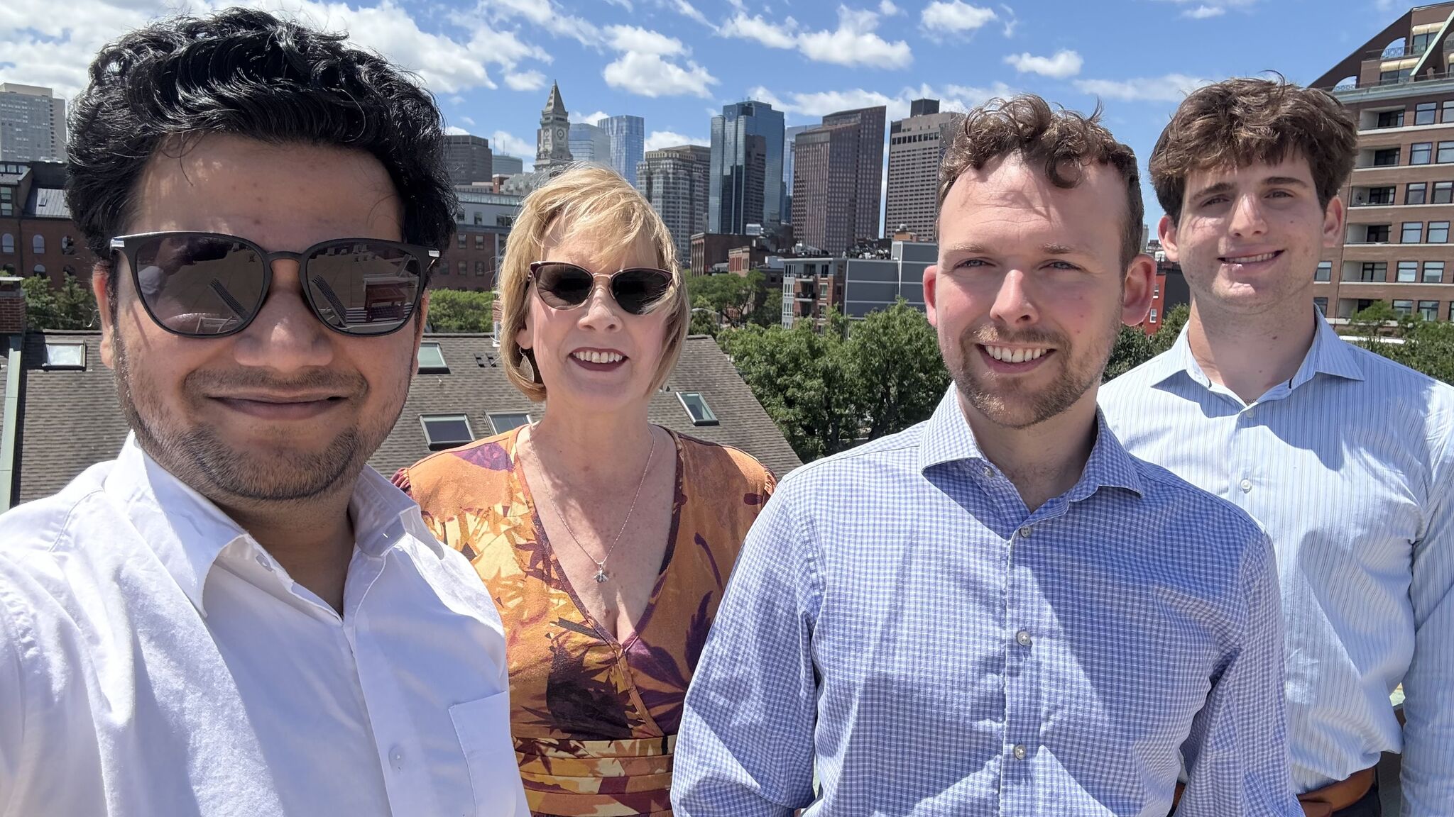 Four people smiling with the Boston skyline in the background