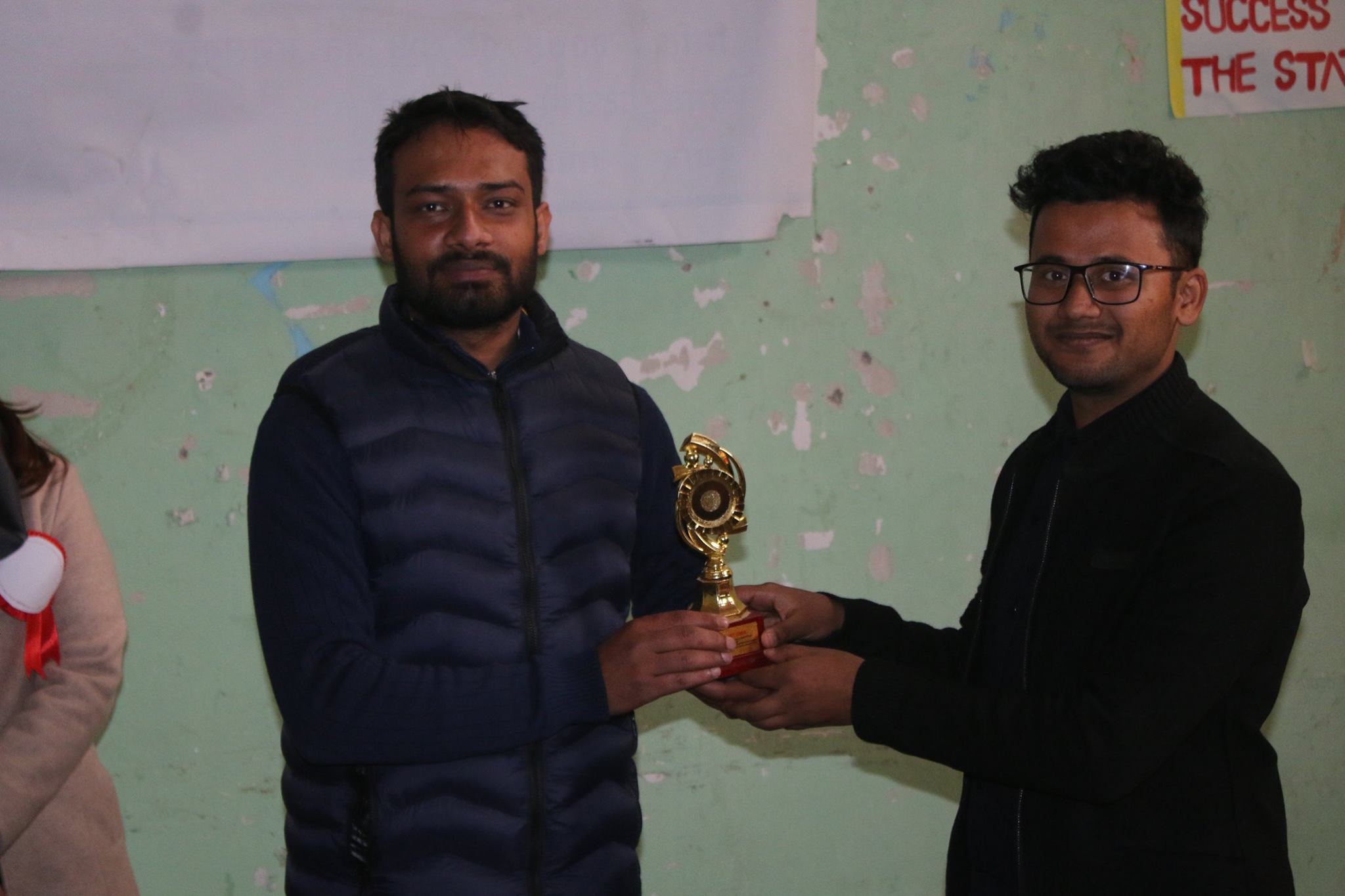 Two people exchanging a trophy at a youth competition event in Nepal